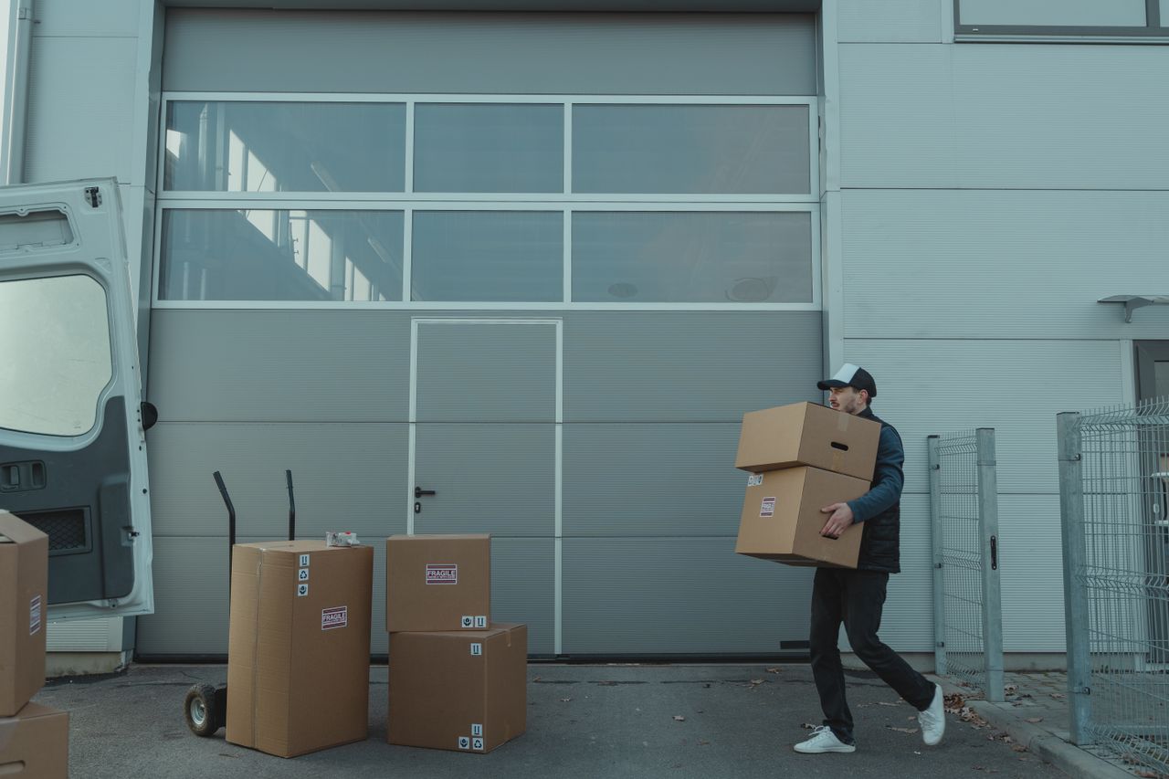 Services-03 A delivery person carrying cardboard boxes outside a warehouse facility.