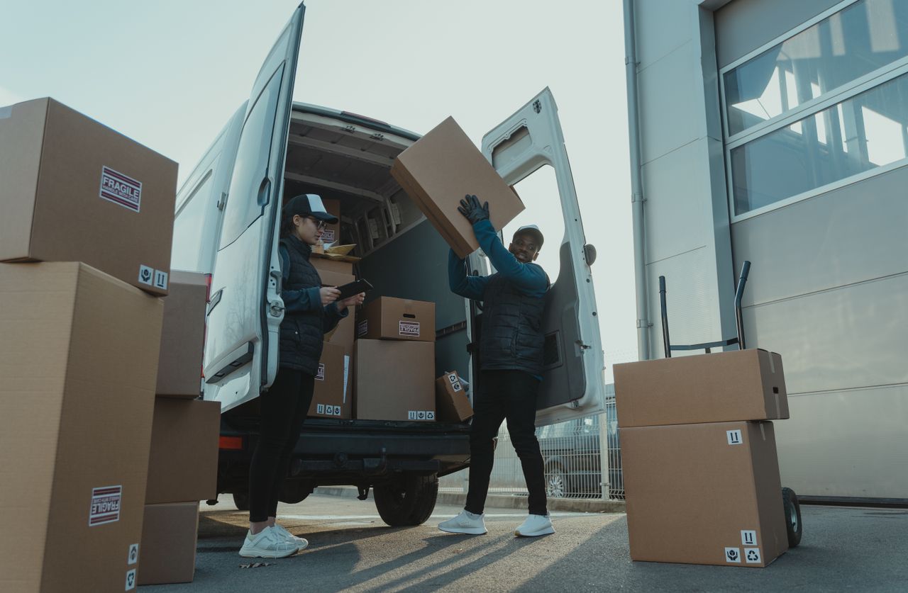 creative Workers loading boxes into a delivery van at a warehouse facility outdoors.