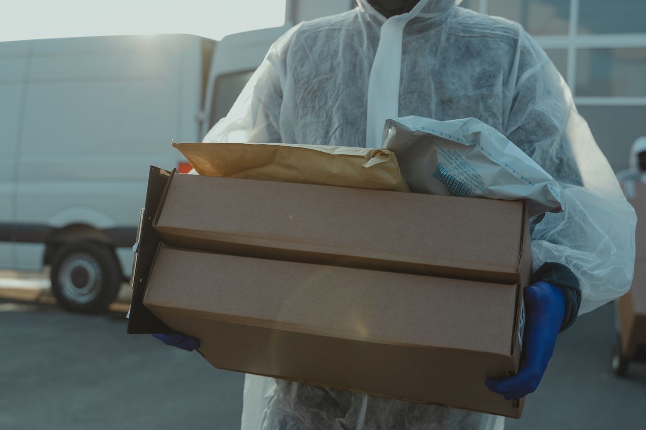 Services-01 A delivery person in PPE carrying packages outside during COVID-19 pandemic.